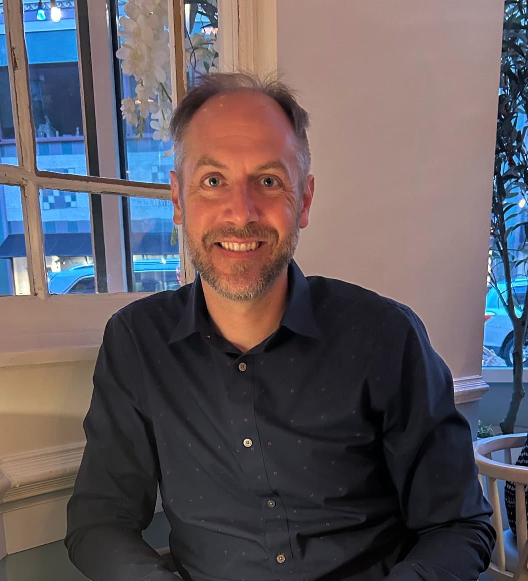 Smiling middle-aged man with a beard wearing a dark blue shirt in a restaurant.