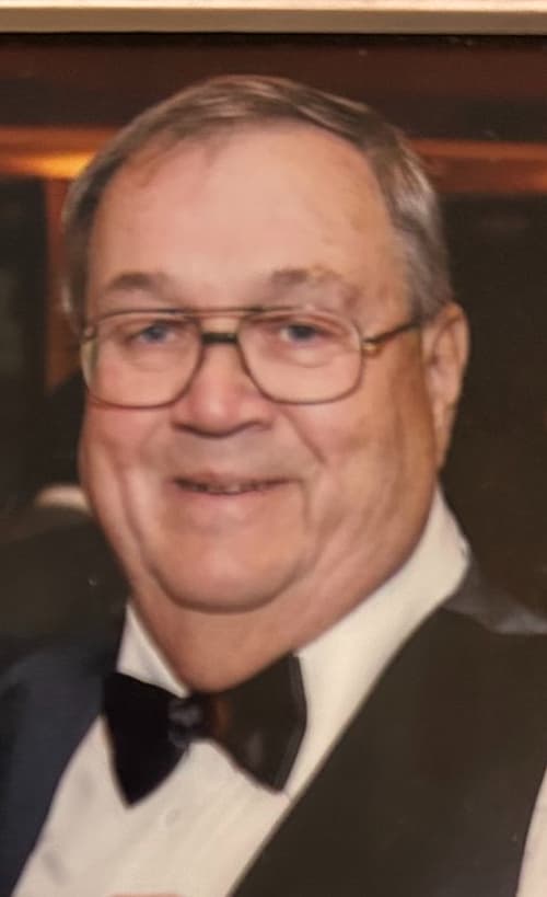 A smiling older man with glasses wearing a white shirt and black bow tie.